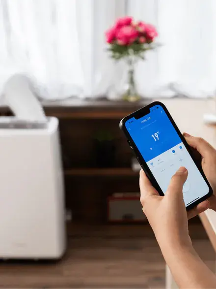 Zdjęcie przedstawia osobę trzymającą w ręce telefon z aplikacja do ustawień klimatyzatora.